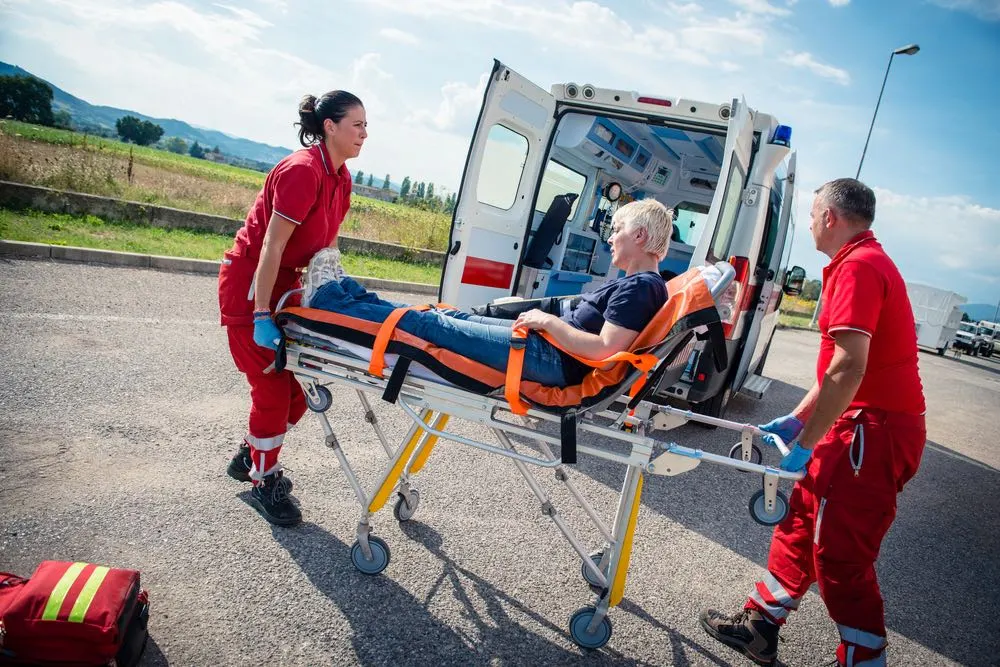 Photo of emergency responders with an ambulance assisting an injured person, highlighting catastrophic injuries from wrong way accidents.